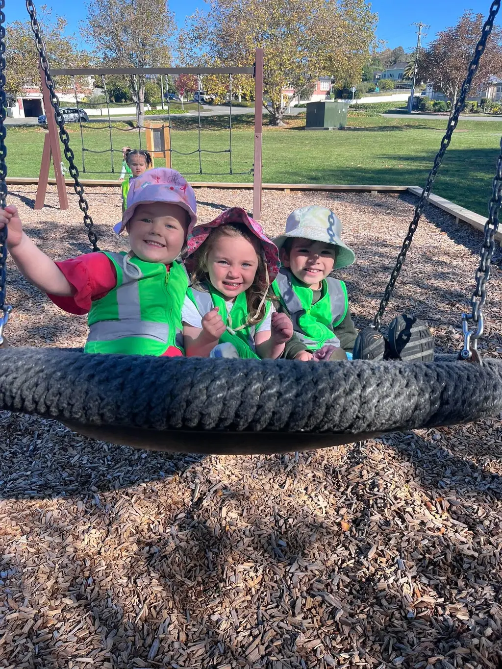 Three tamariki smiling together on a playground swing